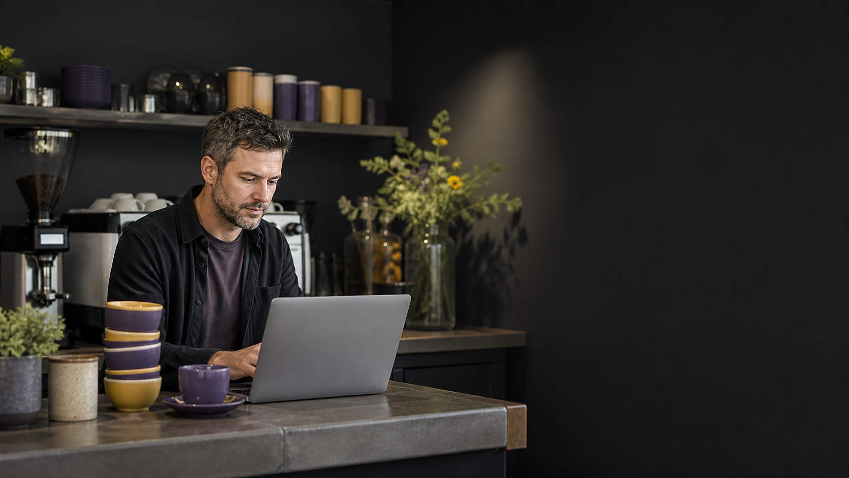 An independent cafe owner working on a laptop behind a coffee-shop counter